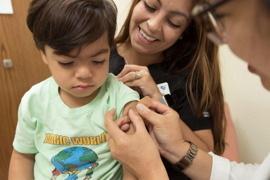 Woman with young boy as he gets a Band-Aid on placed on his arm by medical professional.