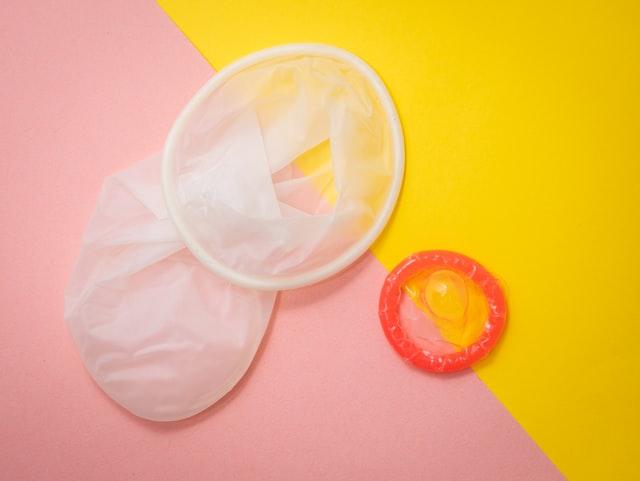 Two unwrapped condoms again against a yellow and pink background.